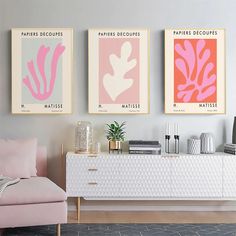 three pink and yellow posters hang on the wall above a white dresser in a living room