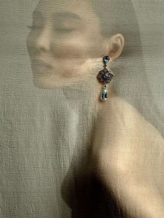 a woman's face is reflected in the glass behind her earring, which has a blue bead hanging from it