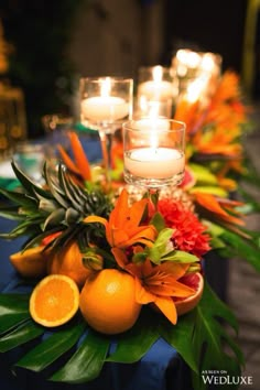 an arrangement of oranges, pineapples and candles on a blue table cloth