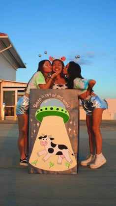 three girls hugging each other while standing in front of a sign with a cow on it