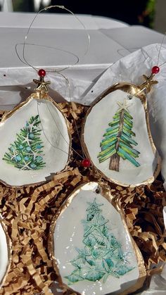 four christmas ornaments are sitting in a box on some wood shavings and decorated with gold trim