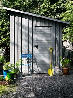 a small shed with a yellow shovel next to it and some potted plants on the side