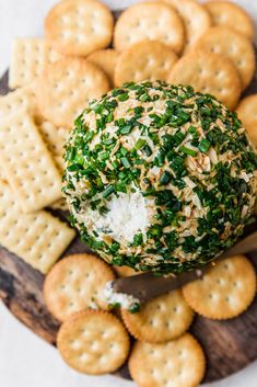 crackers and cheese are arranged on a wooden platter next to crackers that have been dipped with parsley