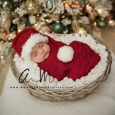 a baby wearing a santa hat and sleeping in a basket next to a christmas tree