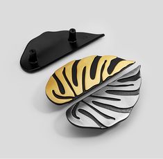 two black and gold leaf shaped brooches next to each other on a gray surface