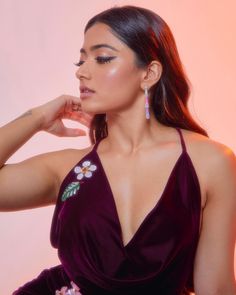 a woman in a purple dress with flowers on her chest and earrings, posing for the camera