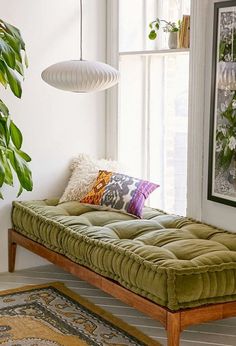 a green futon bed sitting in front of a window next to a potted plant