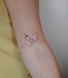 a woman's arm with a small tattoo of a dog holding a heart on it