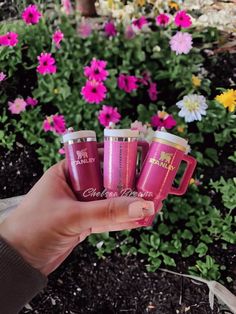 three pink coffee mugs are held in front of some flowers