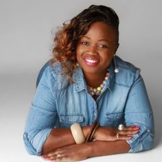 a woman sitting on the floor with her arms crossed, smiling at the camera and wearing a denim shirt