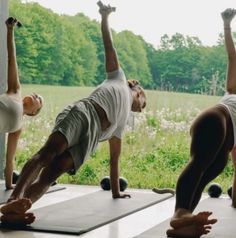 three people are doing yoga outside on their mats in front of some grass and trees