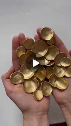 two hands holding gold discs in front of a white wall