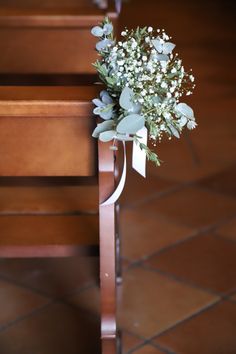 a bouquet of flowers tied to the back of a wooden church pew with white ribbon