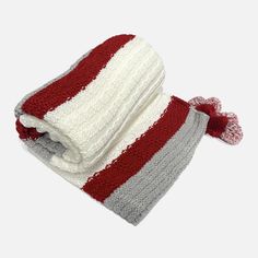 a red, white and grey knitted blanket with tassels on it's ends