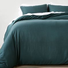 a bed with green sheets and pillows on top of wooden floor next to white wall