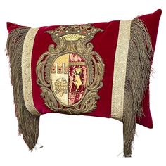 a red and gold decorative pillow with fringes on the bottom, featuring a coat of arms