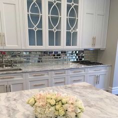 a white kitchen with marble counter tops and cabinets in front of the sink is filled with flowers