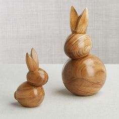 two wooden toys sitting next to each other on a white tableclothed surface, one is made out of wood and the other has ears shaped like rabbits