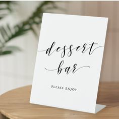 a sign that says dessert bar on it sitting on a table next to a potted plant