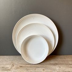 a stack of white plates sitting on top of a wooden table next to a gray wall