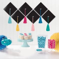 an assortment of desserts and decorations on a white table with black graduation hats hanging from the ceiling