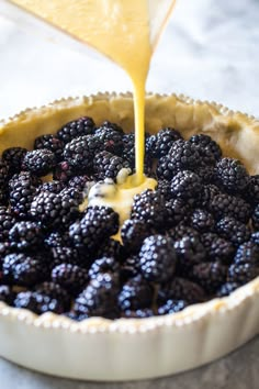 a pie pan filled with fresh blackberries being drizzled with orange juice