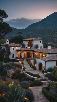 a large house with lots of plants and trees in front of it at night time