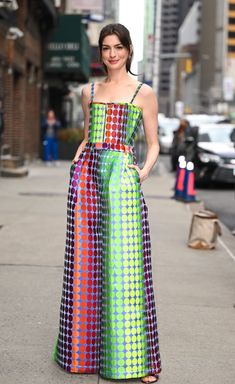 a woman in a multicolored dress is walking down the street with her hand on her hip