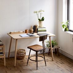 a desk with some books on it next to a window and a potted plant