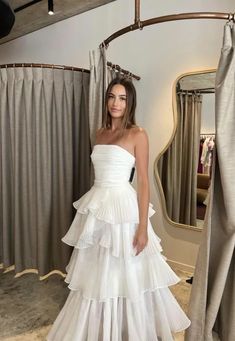 a woman standing in front of a mirror wearing a white dress with tiered layers