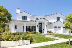 a white house with lots of windows and bushes in front of it on a sunny day