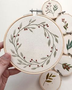 a hand is holding a embroidery hoop with red berries and green leaves on it