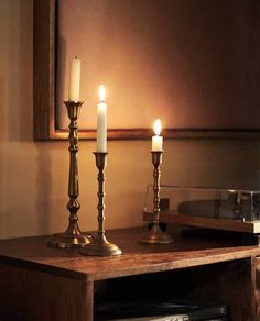 three candles are lit on a wooden table in front of a mirror and record player