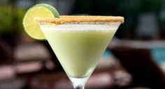 a green drink in a martini glass with a lime slice on the rim and sugary crumbs