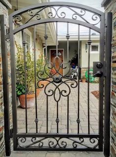 an iron gate in front of a brick house with potted plants on the side