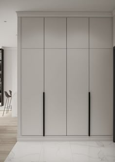 an empty room with white cupboards and black chairs on the far wall, in front of a dining table