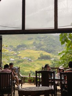 people are sitting at tables in front of a window overlooking the mountains and rice fields