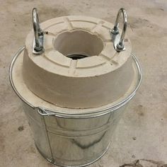 a metal bucket with two handles on the top and one handle in the middle, sitting on concrete