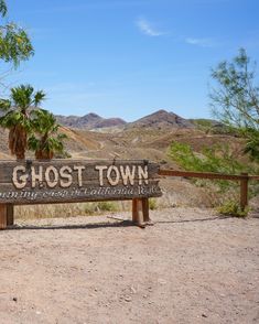 a wooden sign sitting on the side of a dirt road next to a forest filled with palm trees