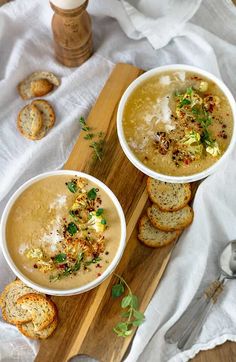 two bowls filled with soup on top of a wooden cutting board next to some bread