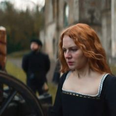 a woman with red hair is standing in front of an old building and looking at something