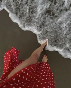 a woman in a red polka dot dress laying on the beach