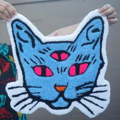 a person holding up a cat shaped rug with eyes painted on it's face