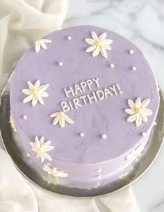 a purple birthday cake with white daisies on it and the words happy birthday written in frosting