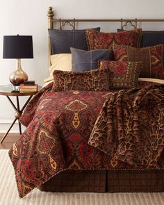 a bed covered in brown and red comforter next to a night stand