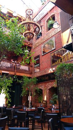 the inside of a restaurant with tables, chairs and plants hanging from the ceiling above