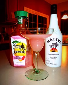 a pink drink sitting on top of a counter next to two bottles of alcohol and a shaker