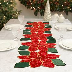 the table is decorated with red flowers and green leaves on it, along with white plates