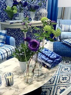 a living room filled with furniture and flowers on top of a coffee table in front of a blue wall