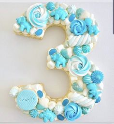 the number three is decorated with blue and white icing, flowers and seashells